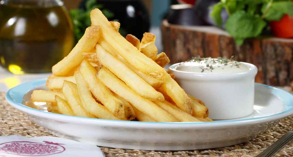 Tigela de batatas fritas com molho cremoso de alho, servidas em uma cozinha aconchegante e iluminada.