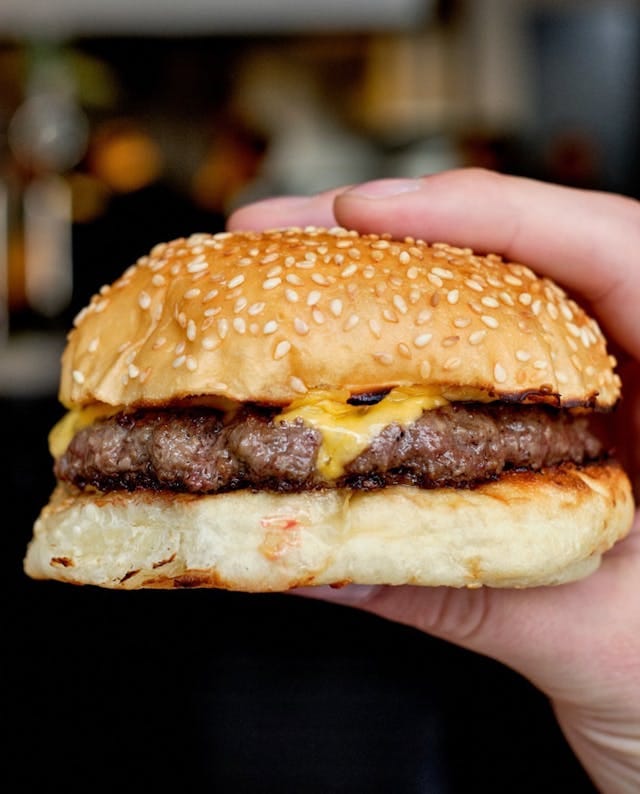 Hambúrguer simples com um bife, cebola, molho de mostarda e pão de gergelim.