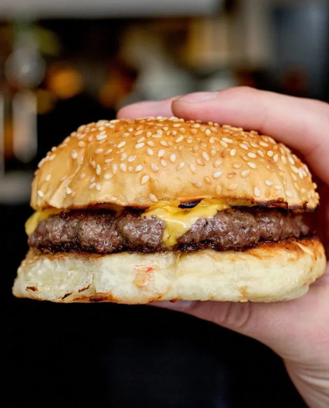 Hambúrguer simples com um bife, cebola, molho de mostarda e pão de gergelim.