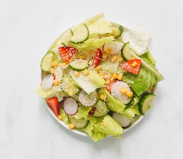 Prato de salada colorida com folhas verdes, pepino fatiado, rabanete em rodelas finas e morangos frescos