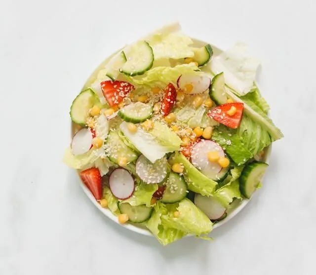 Prato de salada colorida com folhas verdes, pepino fatiado, rabanete em rodelas finas e morangos frescos